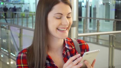 Young-beautiful-woman-standing-in-shopping-mall-smiling.-Using-her-smartphone,-talking-with-friends