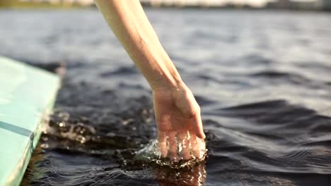 At-sunset,-close-up-the-hand-of-a-girl-moving-through-the-water