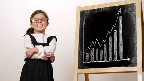 A-happy-girl-dressed-as-a-teacher-in-front-of-a-small-blackboard-holds-her-arms-folded-and-smiles.