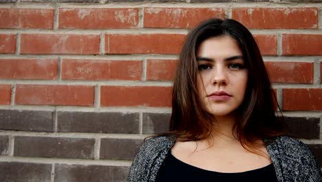 Portrait-of-a-young-serious-woman-against-a-brick-wall.-Slow-motion-shot.