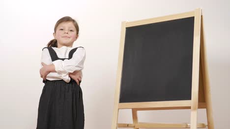 A-happy-girl-dressed-as-a-teacher-in-front-of-a-small-blackboard-holds-her-arms-folded-and-smiles.