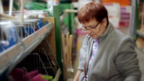 An-elderly-woman-in-a-hypermarket-in-the-Department-tools-chooses-necessary-equipment-for-the-garden