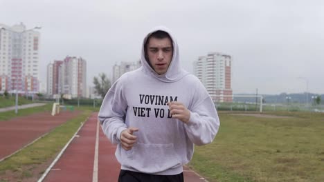 Young-man-training-at-stadium-in-morning.-Boxer-running-in-hoodie-outdoors