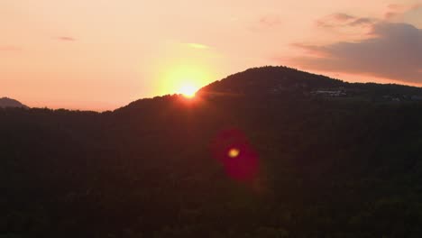 AÉREA:-Volando-sobre-el-denso-bosque-iluminado-por-la-impresionante-puesta-de-sol-naranja.