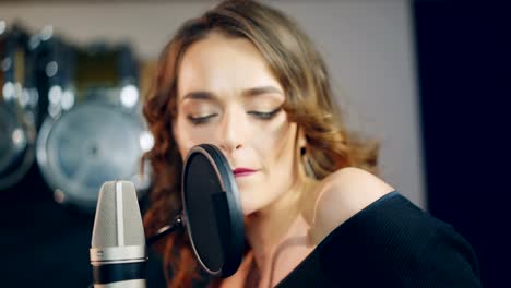 beautiful-singer-with-curly-hair-is-singing-a-song-in-an-audio-recording-studio-on-the-background-of-professional-equipment.