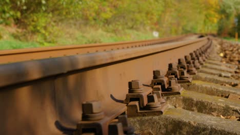 A-close-up-view-of-the-large-screws-securing-the-train-tracks-during-a-sunny-day-while-slowly-passing-forward-looking-from-the-bottom-of-the-stones.