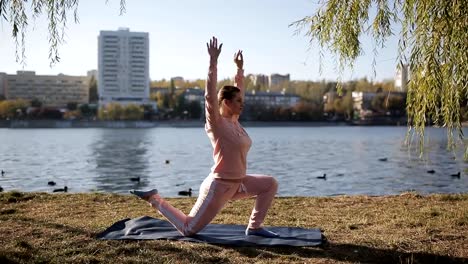 Hermosa-chica-en-un-chándal-en-el-paseo-marítimo-de-la-ciudad-hace-yoga.