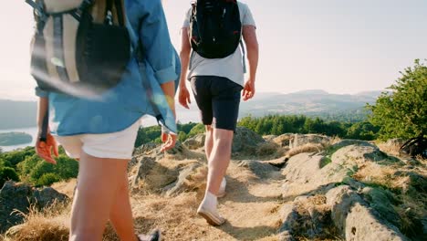 Slow-Motion-Rear-View-Shot-Of-Young-Couple-Standing-At-Top-Of-Hill-Looking-At-Beautiful-Countryside-On-Hike-Through-Lake-District-In-UK