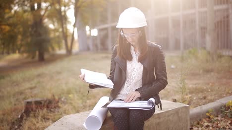 Studentin-in-einem-Helm-und-Schutzbrille-auf-der-Baustelle-untersucht-die-technische-Dokumentation