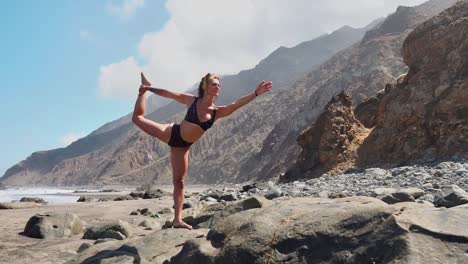 hübsche-blondes-Mädchen-in-schwarzen-Top-entspannt-sich-in-Yoga-Pose-Lotus-auf-lila-Matte-gegen-die-Wellen-des-Ozeans,-die-auf-Felsen