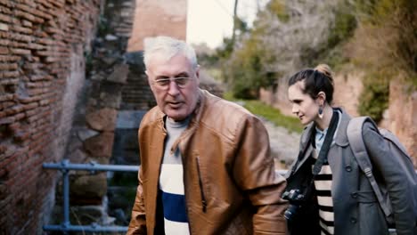 Young-European-woman-and-senior-man-enjoying-walking-tour-around-old-ruins-of-Ostia,-Italy-during-family-vacation-trip.