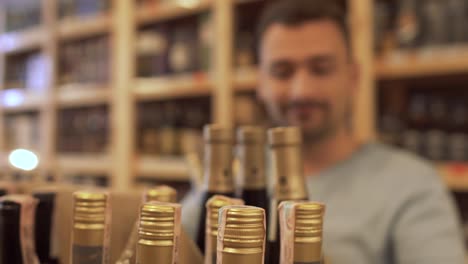 Joyful-guy-taking-a-few-bottles-in-his-hands-and-happily-go-away.-Guy-who-choosing-the-wine-in-the-store-is-out-of-focus.