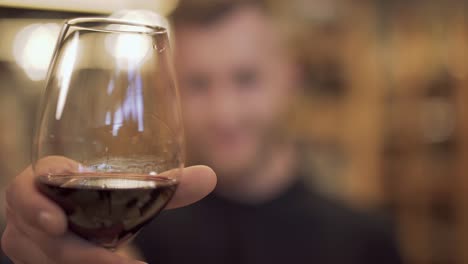 Closeup-de-un-vaso-de-vino-que-tiene-a-un-chico-guapo.-El-enfoque-se-mueve-de-la-Copa-de-vino-para-el-atractivo-chico-barbudo.-Flujos-de-vino-abajo-de-los-bordes-de-la-Copa-de-vino.