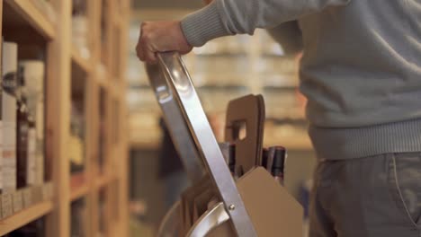 Man-hands-close-up-put-wine-bottles-on-the-shelfs-Man-is-using-ladder-to-reach-higher