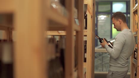 Handsome-man-looking-the-inscriptions-on-the-bottle-of-wine.-Customer-is-choosing-drink-in-alcohol-shop.