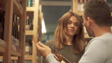 Pretty-girl-gives-advice-to-the-visitor-of-the-liquor-store.-Customers-choosing-drink-in-alcohol-shop.