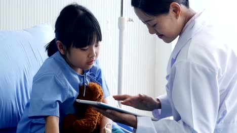 Doctor-visiting-Little-Girl-in-the-Hospital,-Little-Girl-looking-to-tablet-with-doctor-together-in-hospital.-People-with-Technology,-Healthcare-and-Medical-Concept.