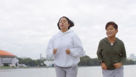 Athletic-Asian-Mother-and-Son-Jogging-Outdoors-along-Urban-Riverside