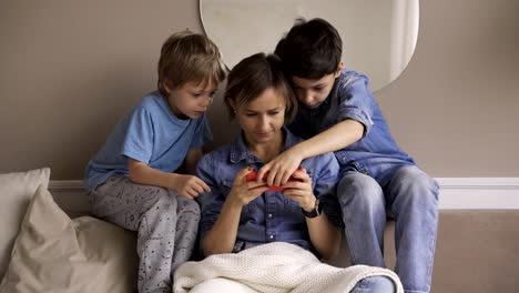 Young-caucasian-woman-with-two-child-have-fun-using-smartphone-relaxing-on-couch,-happy-boys-enjoy-spending-time-at-home-with-mom.-Video-games