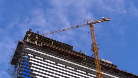 Kran-auf-einer-Baustelle-gegen-den-blauen-Himmel-baut-einen-neuen-Wolkenkratzer.-Gebäudebau