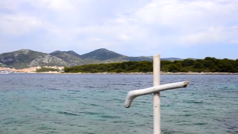 Wooden-christian-white-cross-on-rocky-shore-of-blue-sea.-Seacoast-of-Hvar-island-and-harbour-in-old-town-Hvar.