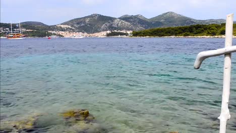 Christlichen-weißen-Holzkreuz-am-felsigen-Ufer-des-blauen-Meeres.-Küste-der-Insel-Hvar-und-Hafen-in-der-Altstadt-von-Hvar.