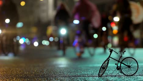 Lot-of-cyclists-ride-during-night-cycling-bike-parade-in-blur-by-illuminated-night-city-street-against-background-of-small-scale-model-of-bicycle.-Crowd-of-people-on-bike.-Bike-traffic.-Concept-sport-healthy-lifestyle.-Bright-shining-lights.-Low-angle