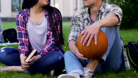 Girl-with-book,-guy-with-basketball-ball-sitting-grass-and-talking,-relationship