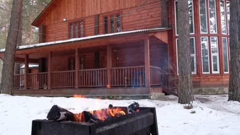 Panoramic-video-of-open-fire-in-iron-brasier-barbecue-with-cottage-on-background