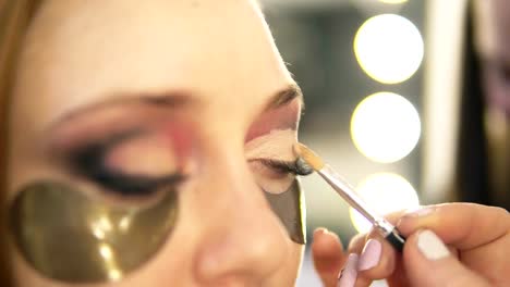 Make-up-Künstler-setzen-auf-helle-Augen-Schatten-auf-des-Modells-Auge.-Hautnah.-Patches.-Seitenansicht