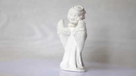 white-angel-statue-revolves-on-a-stand-against-a-white-wooden-wall.-FullHD-format-video