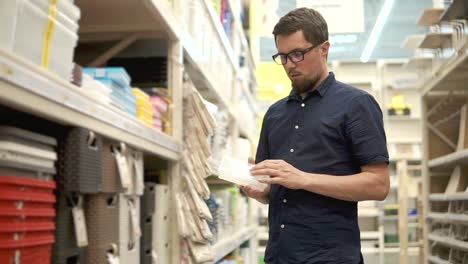 Householder-is-comparing-two-plastic-boxes-in-supermarket,-standing-near-shelves