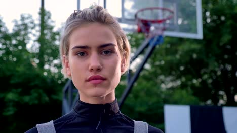 Serious-gorgeous-female-basketball-player-looking-at-camera,-standing-in-park,-hoop-in-background