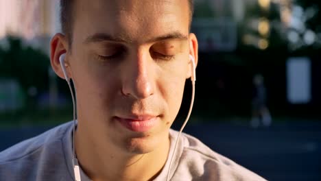 Porträt-der-schönen-jungen-Mann-Musik-über-Kopfhörer-hören-und-Blick-in-die-Kamera,-Personen,-spielen-unter-freiem-Himmel-Hintergrund