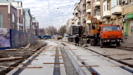 Straßenbahnschienen-auf-der-Stufe-der-deren-Entladung-von-LKW-mit-einem-Kran-auf-Betonplatten-auf-der-Straße-Zeitraffer