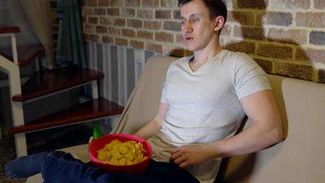 Hombre-joven-con-cerveza-y-patatas-fritas-en-frente-de-la-TV