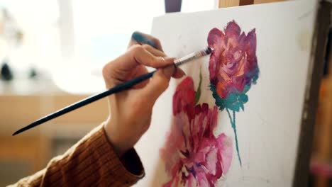 Close-shot-of-dirty-girl's-hand-holding-brush-and-painting-flowers-beautiful-still-life-picture-working-in-workshop-alone.-Creativity-and-art-concept.