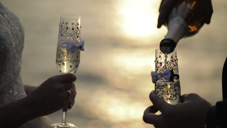 Champagne-is-poured-from-bottel-into-a-wedding-glass-on-the-background-of-the-sea.-Lovely-groom-and-bride.-Slow-motion