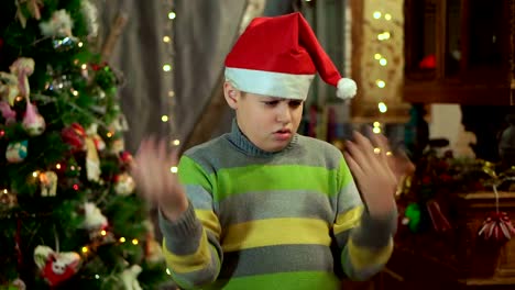El-niño-con-el-suéter-y-sombrero-de-Santa-Claus-es-molesto-y-ofendido.-No-tiene-ningún-regalo.-Contra-el-fondo-de-luces-de-Navidad