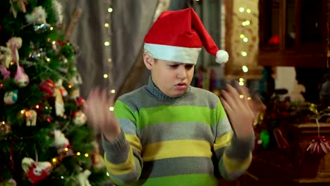 The-boy-in-the-sweater-and-the-hat-of-Santa-Claus-is-upset-and-offended.-He-has-no-gift.-Against-the-background-of-Christmas-lights