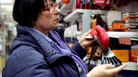 Eine-reife-Frau-wählt-eine-Bürste-mit-Schaber-im-Supermarkt.