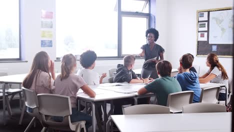 Mujer-alta-escuela-Tutor-permanente-por-mesa-con-estudiantes-enseñando-la-lección