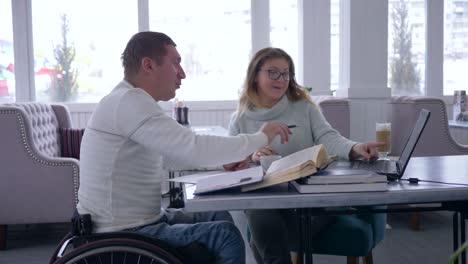 individual-teaching-for-invalid,-educator-woman-into-glasses-conducts-training-for-disabled-men-on-wheelchair-using-smart-computer-technology-and-books