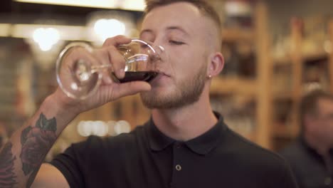 Retrato-de-hombre-atractivo-beber-vino-tinto.-Chico-sonriente-levanta-una-copa-de-vino,-guiños-y-toma-un-sorbo.