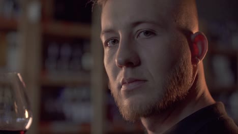 Portrait-of-handsome-male-with-wine-glass-close-up-in-profile-Man-in-dark-room-turns-his-head-and-smiles-on-camera