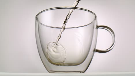 Hot-tea-being-poured-inside-a-glass-in-front-of-white-background-in-slowmotion