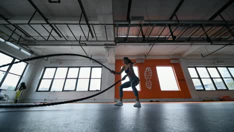 Young-athletic-girl-practicing-battle-rope-exercise-during-a-gym-workout-at-fitness-gym.-Slow-Motion.