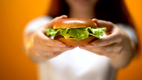 Chica-mostrando-la-hamburguesa-de-carne-de-res-a-cámara,-tentación-por-la-comida-rápida,-poco-saludable-de-comer