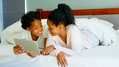 Front-view-of-mid-adult-black-mother-and-daughter-using-digital-tablet-on-bed-in-comfortable-home-4k