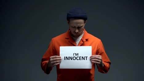 European-imprisoned-male-holding-I-am-innocent-sign-in-cell,-asking-for-justice